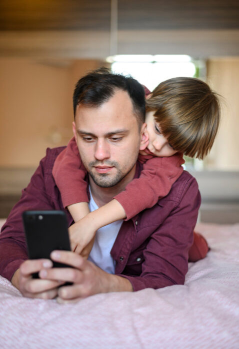 Son hug his father while using his mobile